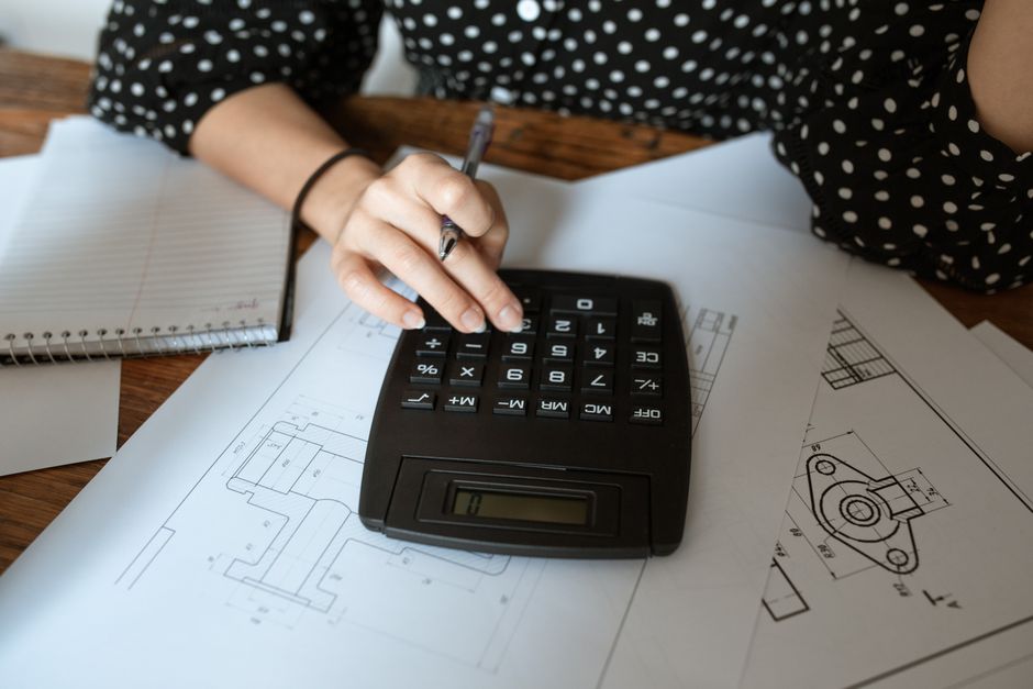 A person's hands using a sleek calculator next to a set of house keys on a wooden desk, illustrating the financial calculation involved in choosing a real estate commission model.