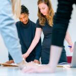 Diverse group of people collaborating around a wooden table, pointing at blueprints and notes for a community project in a...