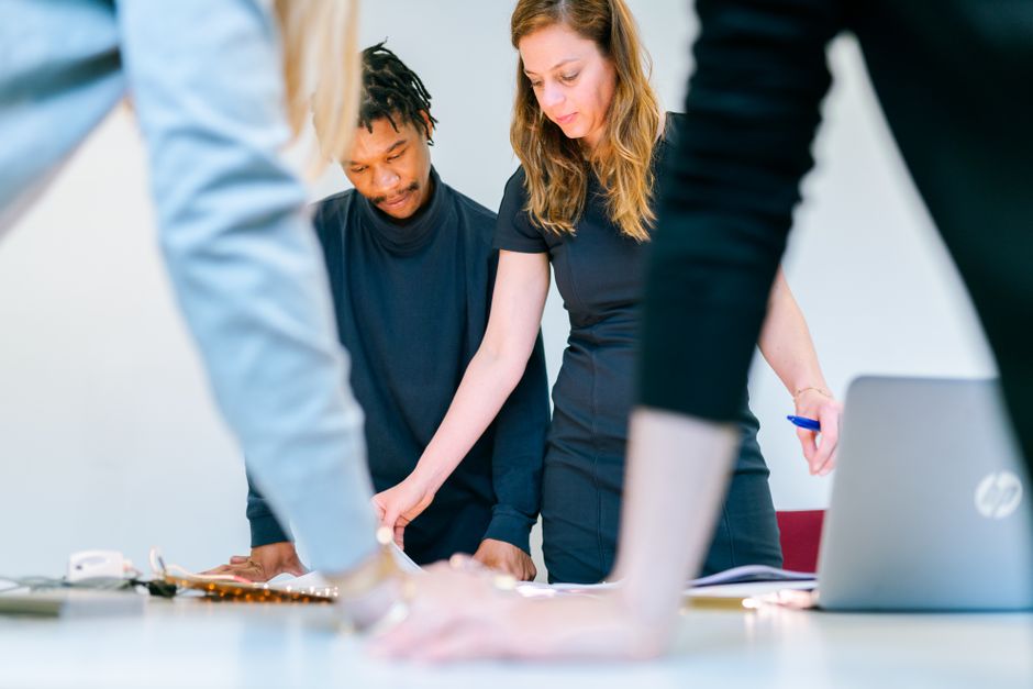 Diverse group of people collaborating around a wooden table, pointing at blueprints and notes for a community project in a...