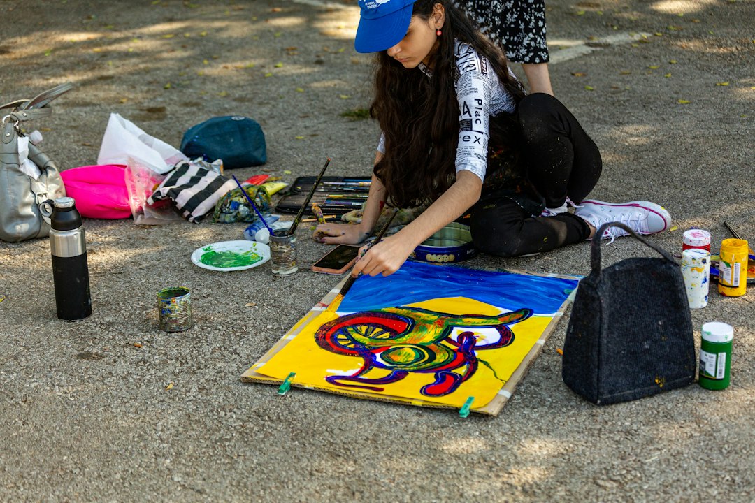 A joyful and diverse group of community members painting a large, colorful mural on an outdoor wall, working together with brushes and rollers.